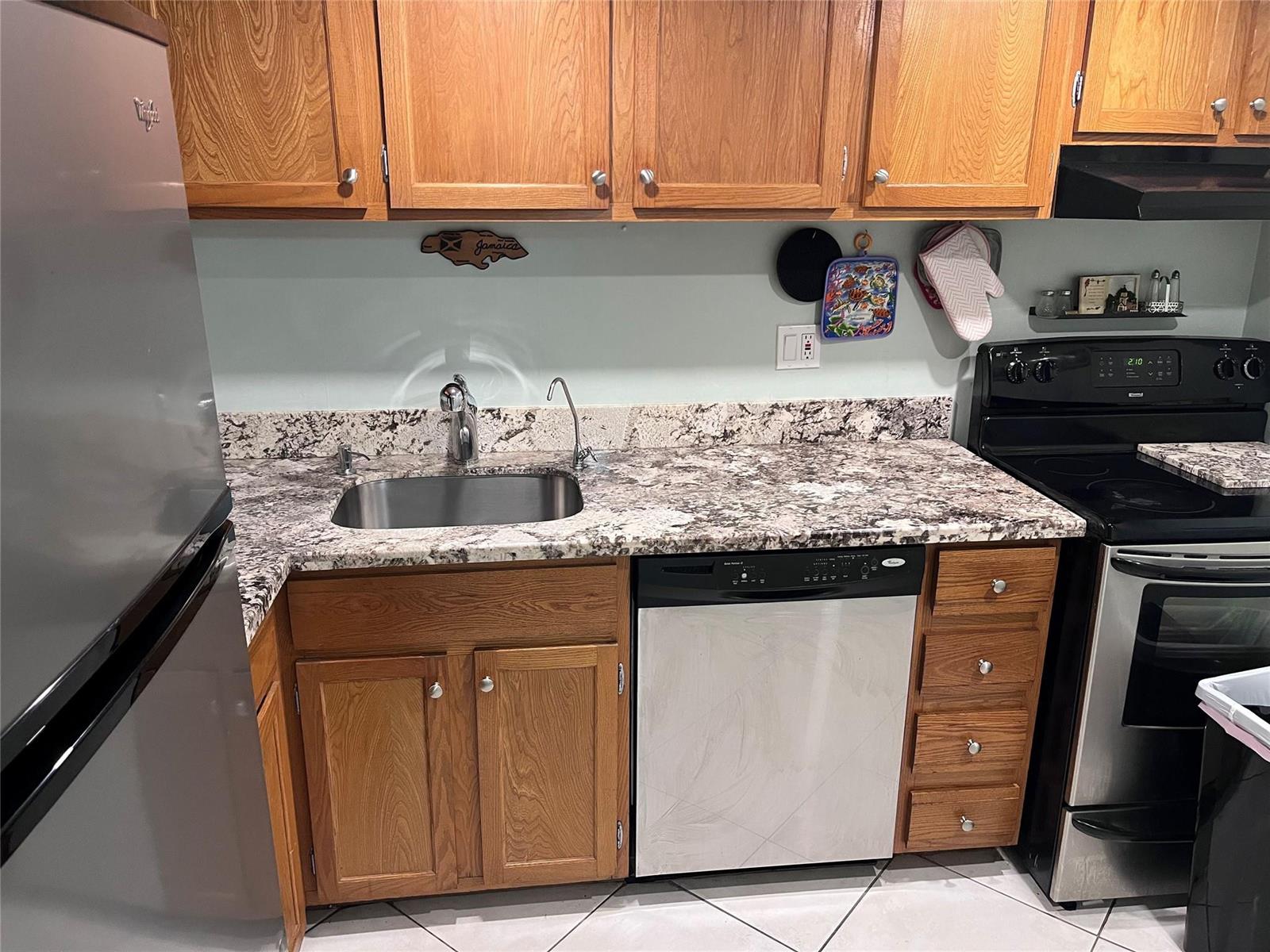 A kitchen features wood cabinets, granite countertops, a stainless steel sink, and black appliances — 3670 N Inverrary Drive # 1F, Lauderhill FL 33319, LAUDERHILL, FL