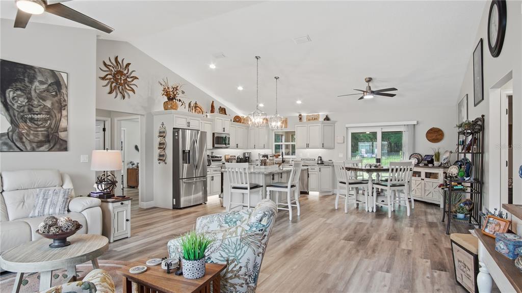 An open-concept kitchen and living area features white cabinetry, wood-look flooring, and vaulted ceilings — 6752 SW 179TH COURT ROAD, DUNNELLON, FL