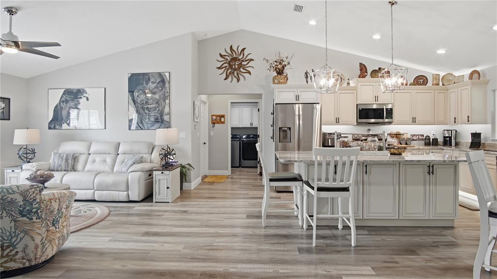 An open-concept living room and kitchen with light wood flooring, white cabinets, and stainless appliances — 6752 SW 179TH COURT ROAD, DUNNELLON, FL