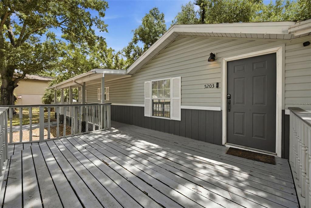 A wooden deck leads to the front entrance of a house with gray siding — 5203 N MENDENHALL DRIVE, TAMPA, FL