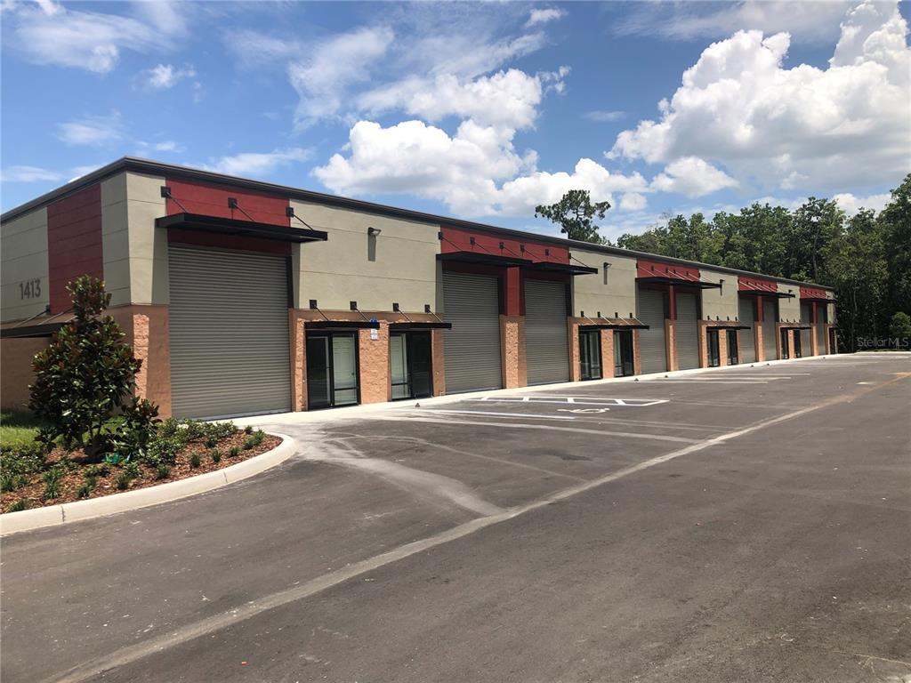 A modern commercial building features multiple roll-up garage doors and glass entryways along a parking lot — 1413 HAMLIN AVENUE UNIT 8, ST CLOUD, FL