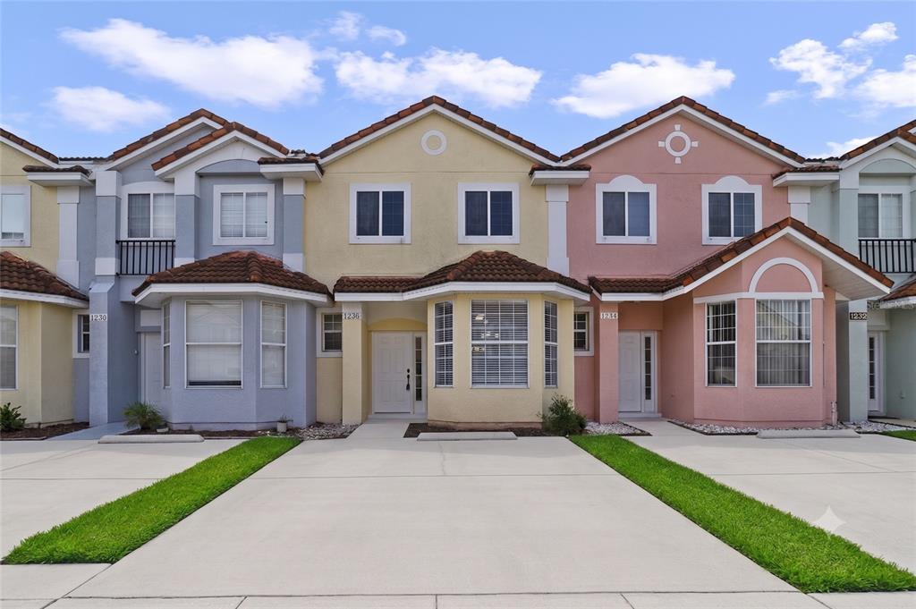 A row of colorful two-story townhouses with concrete driveways and small front lawns — 1236 SOUTH BEACH CIRCLE, KISSIMMEE, FL