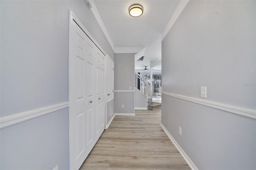 A hallway with light gray walls, white trim, and wood-look flooring leads toward a staircase — 1236 SOUTH BEACH CIRCLE, KISSIMMEE, FL