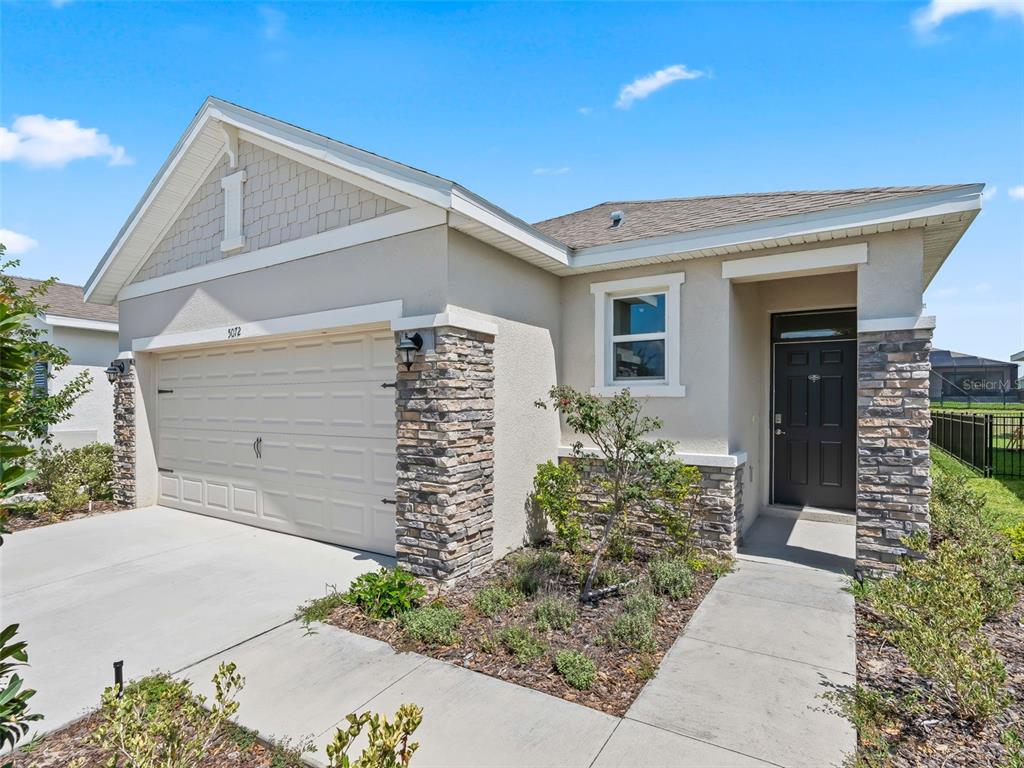 A single-story house exterior features a two-car garage, stone accents, and a dark front door — 5072 STOKES WAY, WILDWOOD, FL
