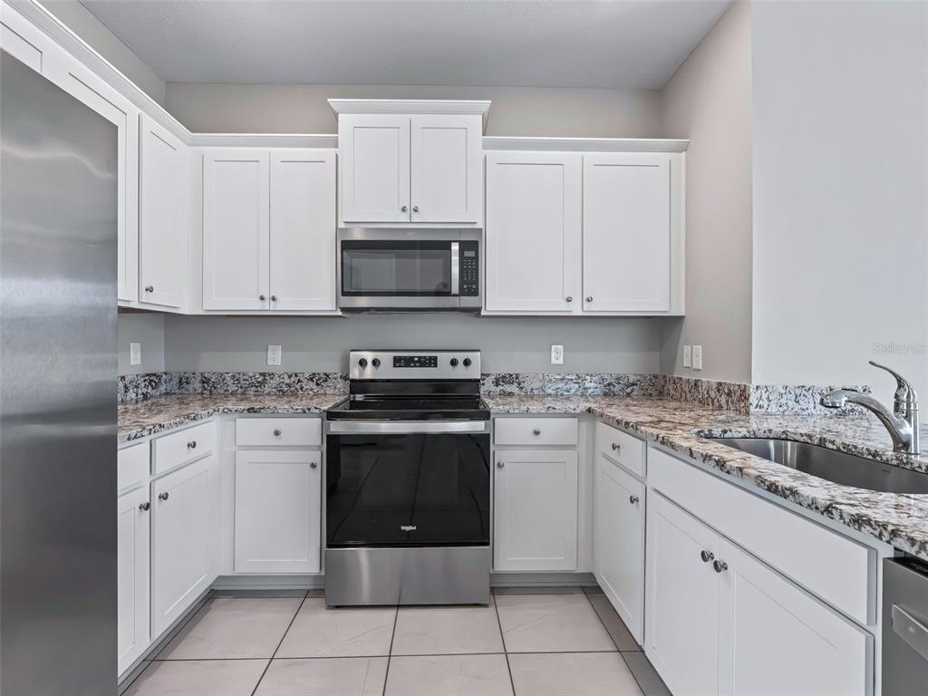 A kitchen features white cabinets, stainless steel appliances, and granite countertops with a tile floor — 5072 STOKES WAY, WILDWOOD, FL