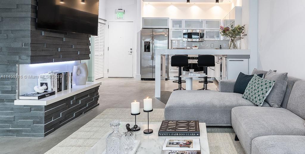 A modern living room features a gray sectional sofa, stone fireplace, and an open kitchen — 2001 Biscayne Blvd # 2104, Miami FL 33137, MIAMI, FL