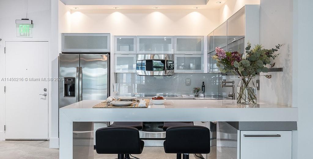A modern kitchen features white cabinetry, stainless steel appliances, and a breakfast bar with stools — 2001 Biscayne Blvd # 2104, Miami FL 33137, MIAMI, FL