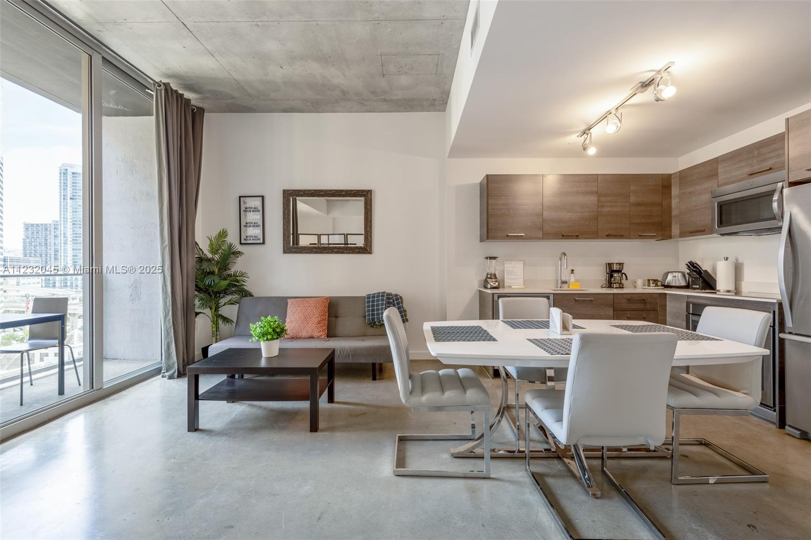 A modern open-concept living and dining area with concrete ceilings, wood cabinets, and balcony access — 151 SE 1st St # 809, Miami FL 33131, MIAMI, FL