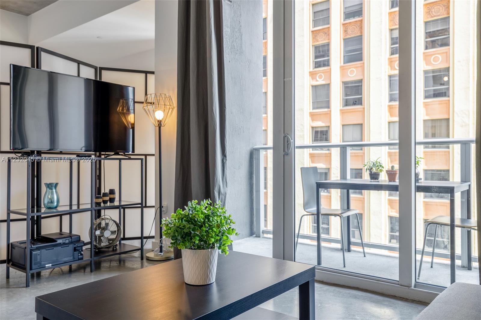 A living room with a television stand, coffee table, and balcony overlooking a city building — 151 SE 1st St # 809, Miami FL 33131, MIAMI, FL