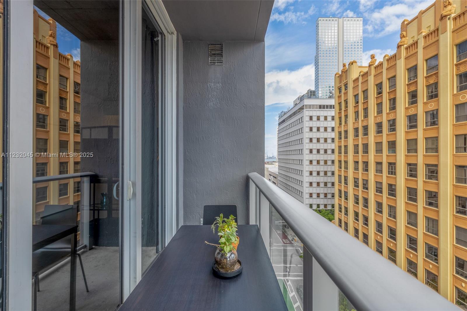 A balcony with a dark table and plant overlooks a city street and nearby buildings — 151 SE 1st St # 809, Miami FL 33131, MIAMI, FL
