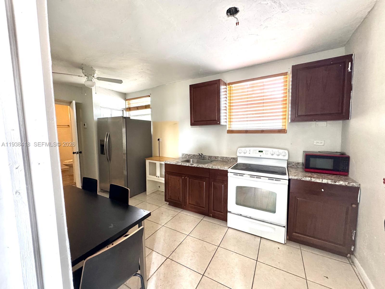 A kitchen features dark wood cabinets, granite countertops, a white stove, and tile flooring — 465 NE 157th Ter # 2, Miami FL 33162, MIAMI, FL