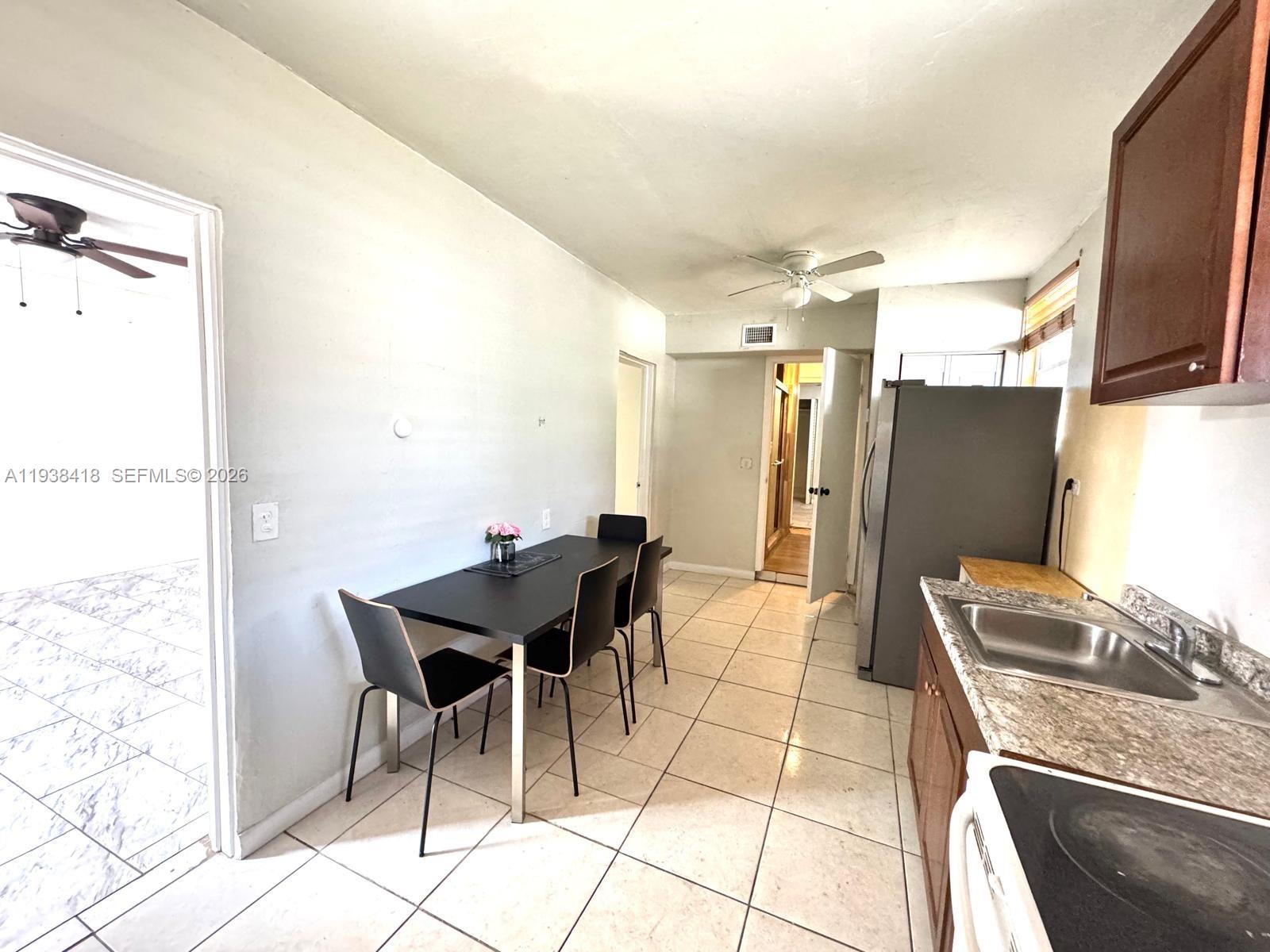 This kitchen features tile flooring, dark wood cabinets, a dining table, and stainless steel appliances — 465 NE 157th Ter # 2, Miami FL 33162, MIAMI, FL