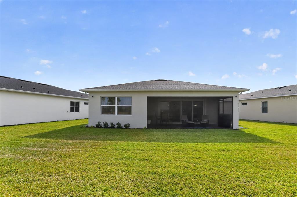 The exterior rear view of a single-story house with a screened-in lanai and lawn — 1599 BELLAGIO LOOP, TAVARES, FL
