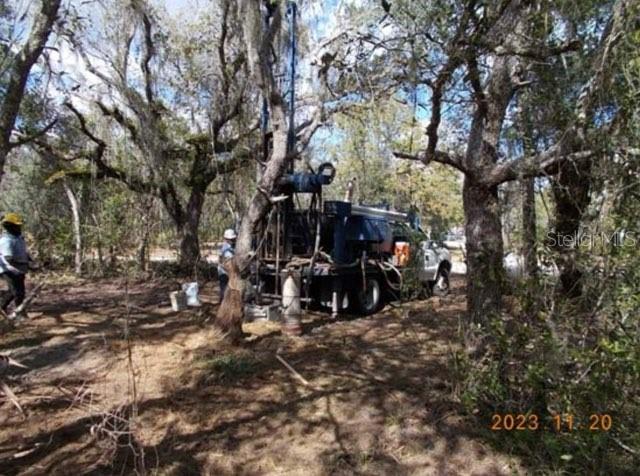 A truck-mounted drilling rig operates in a wooded area with two workers nearby — HAGAR DRIVE, NEW PORT RICHEY, FL