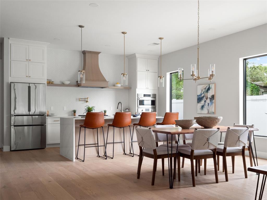 A modern kitchen and dining area with white cabinetry, a wood range hood, and bar seating — 1000 N FOREST AVENUE, ORLANDO, FL