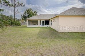 The rear exterior of a beige house features a screened-in porch and a grassy yard — 168 PINE GROVE DRIVE, PALM COAST, FL