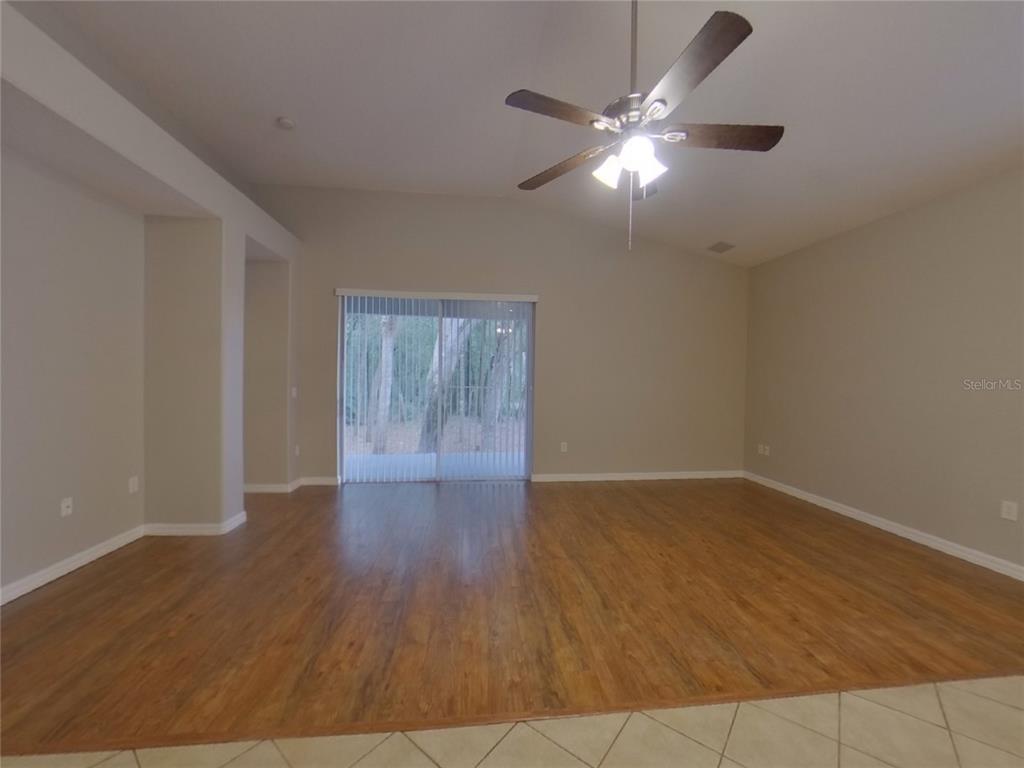 An empty living room features wood-look flooring, a vaulted ceiling with a fan, and sliding doors — 351 FAIRMOUNT PARK COURT, DELAND, FL