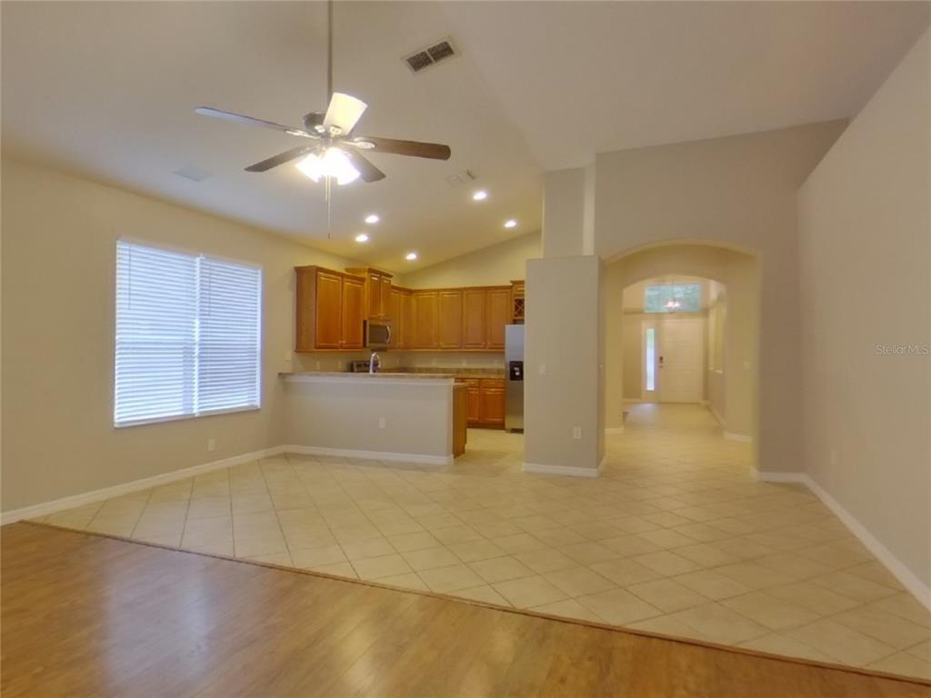 An open-concept kitchen with wood cabinets and tile flooring overlooks a living area — 351 FAIRMOUNT PARK COURT, DELAND, FL
