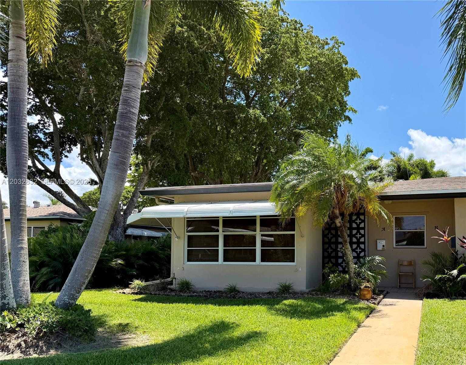 A single-story house exterior features a white metal awning over a window and palm trees — 1042 North Dr # A, Delray Beach FL 33445, DELRAY BEACH, FL