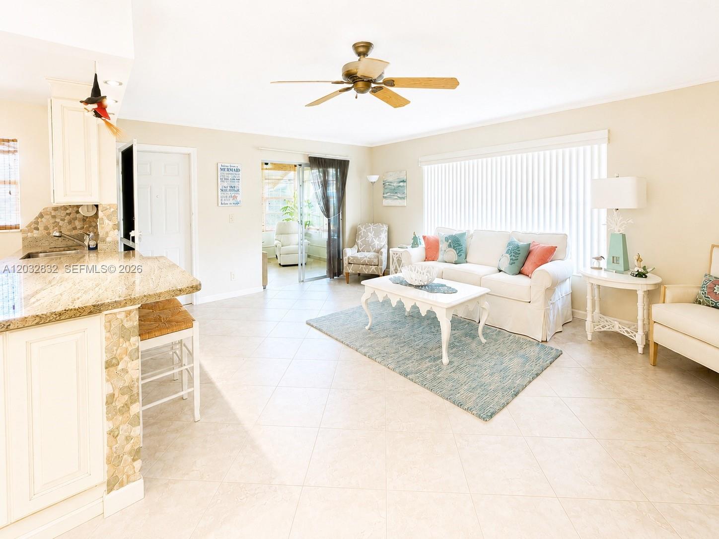 A bright living room features tile floors, a white sofa, and an open kitchen area — 1042 North Dr # A, Delray Beach FL 33445, DELRAY BEACH, FL