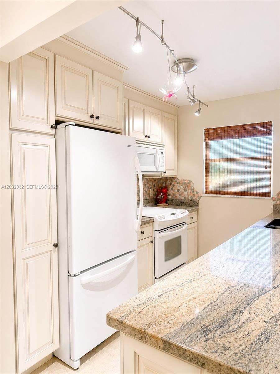A kitchen features cream-colored cabinets, white appliances, and a granite countertop — 1042 North Dr # A, Delray Beach FL 33445, DELRAY BEACH, FL