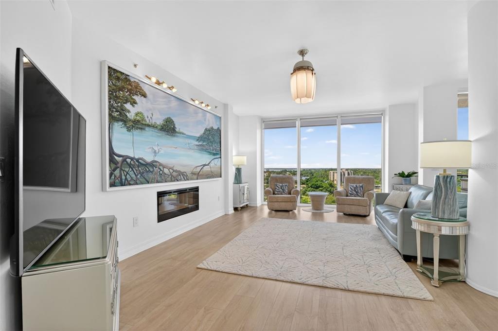 A living room features light wood floors, a fireplace, a large wall painting, and floor-to-ceiling windows — 3426 HANCOCK BRIDGE PARKWAY UNIT 1008, NORTH FORT MYERS, FL