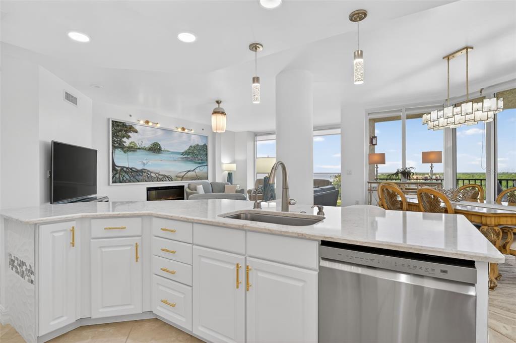 A modern kitchen island with white cabinets and marble countertops overlooks a bright living area — 3426 HANCOCK BRIDGE PARKWAY UNIT 1008, NORTH FORT MYERS, FL