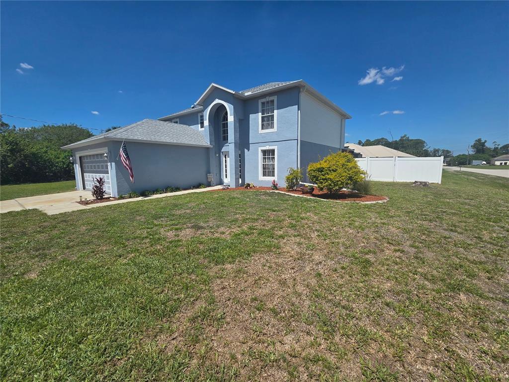 A two-story blue house with a garage and a white fence on a grassy lot — 1389 TIMBERHILL STREET, NORTH PORT, FL