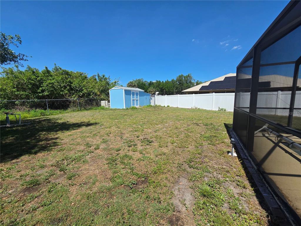 A grassy backyard features a blue storage shed, a white vinyl fence, and a pool enclosure — 1389 TIMBERHILL STREET, NORTH PORT, FL