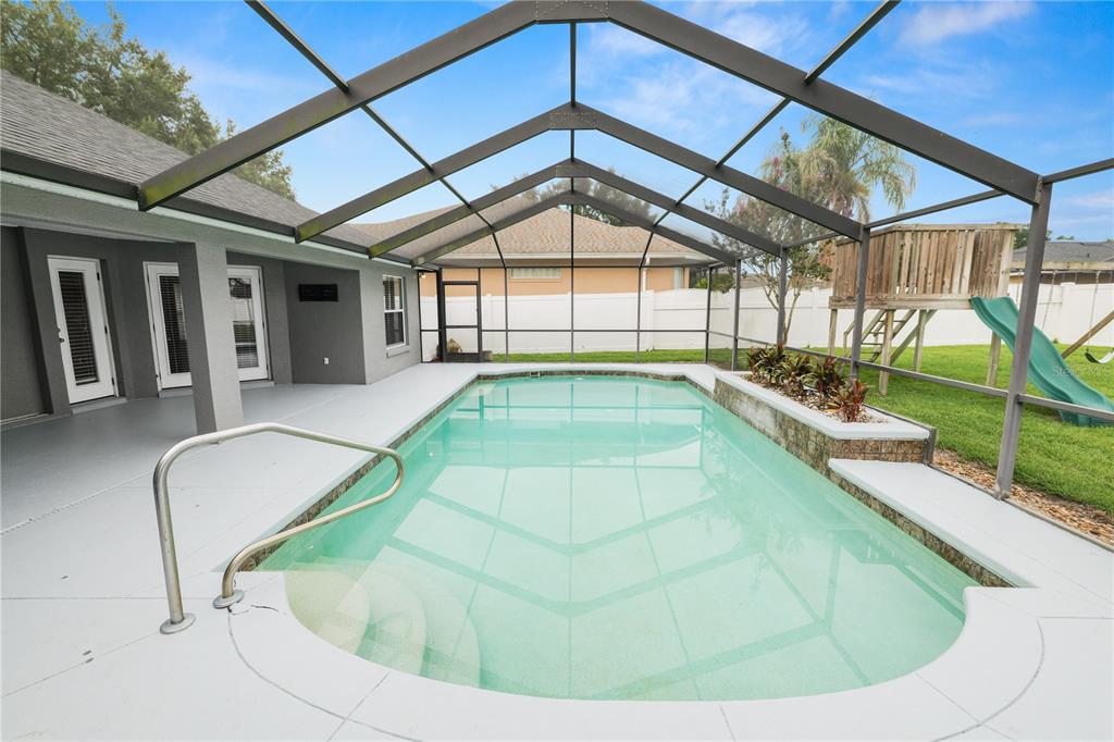 A screened-in patio features a swimming pool with a raised planter and a slide — 3333 HAWKS RIDGE DRIVE, LAKELAND, FL