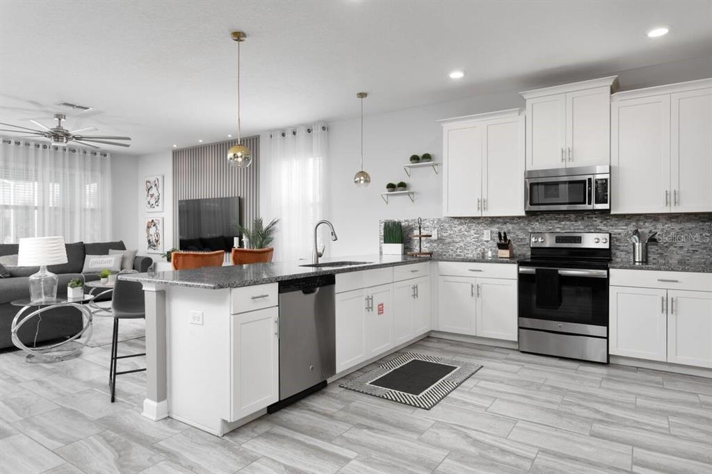 A modern kitchen features white cabinetry, stainless steel appliances, a granite island, and wood-look tile flooring — 9033 HAZARD STREET, DAVENPORT, FL