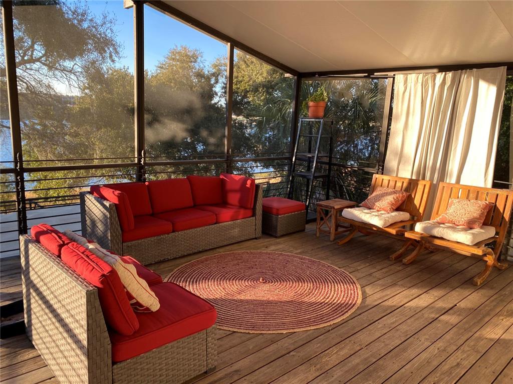 A screened-in wooden porch features red cushioned outdoor furniture and a round area rug — 238 LAKE DRIVE, ORLANDO, FL