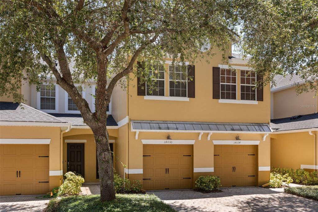 A two-story yellow townhouse with three garage doors and a large tree in front — 14030 SPARKLING COVE LANE UNIT 603, WINDERMERE, FL