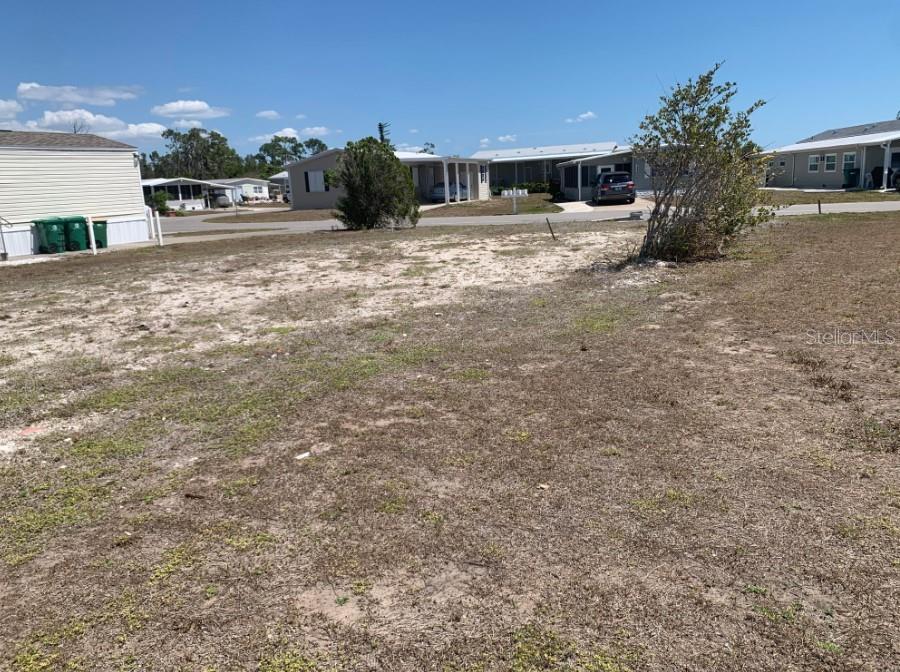 A vacant, sandy residential lot is shown with neighboring manufactured homes in the background — 7360 TISA AVENUE, PORT CHARLOTTE, FL