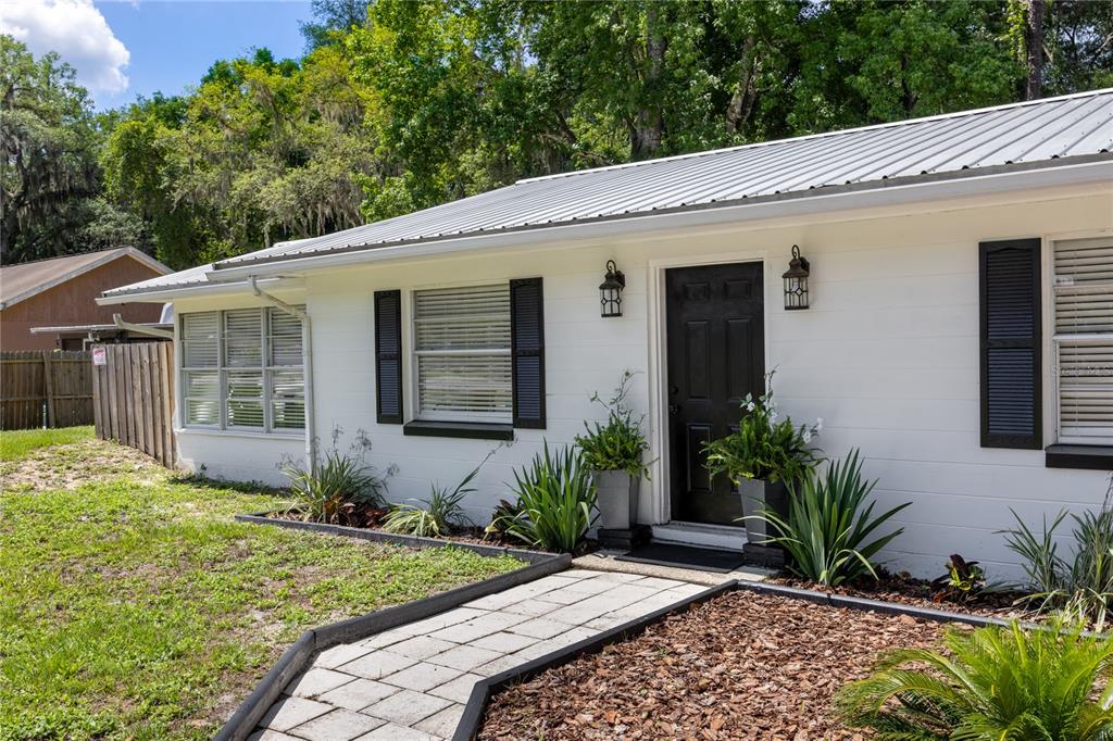 A white house exterior features a black front door, metal roof, and a stone walkway — 113 BROWNS ROAD, SAN MATEO, FL