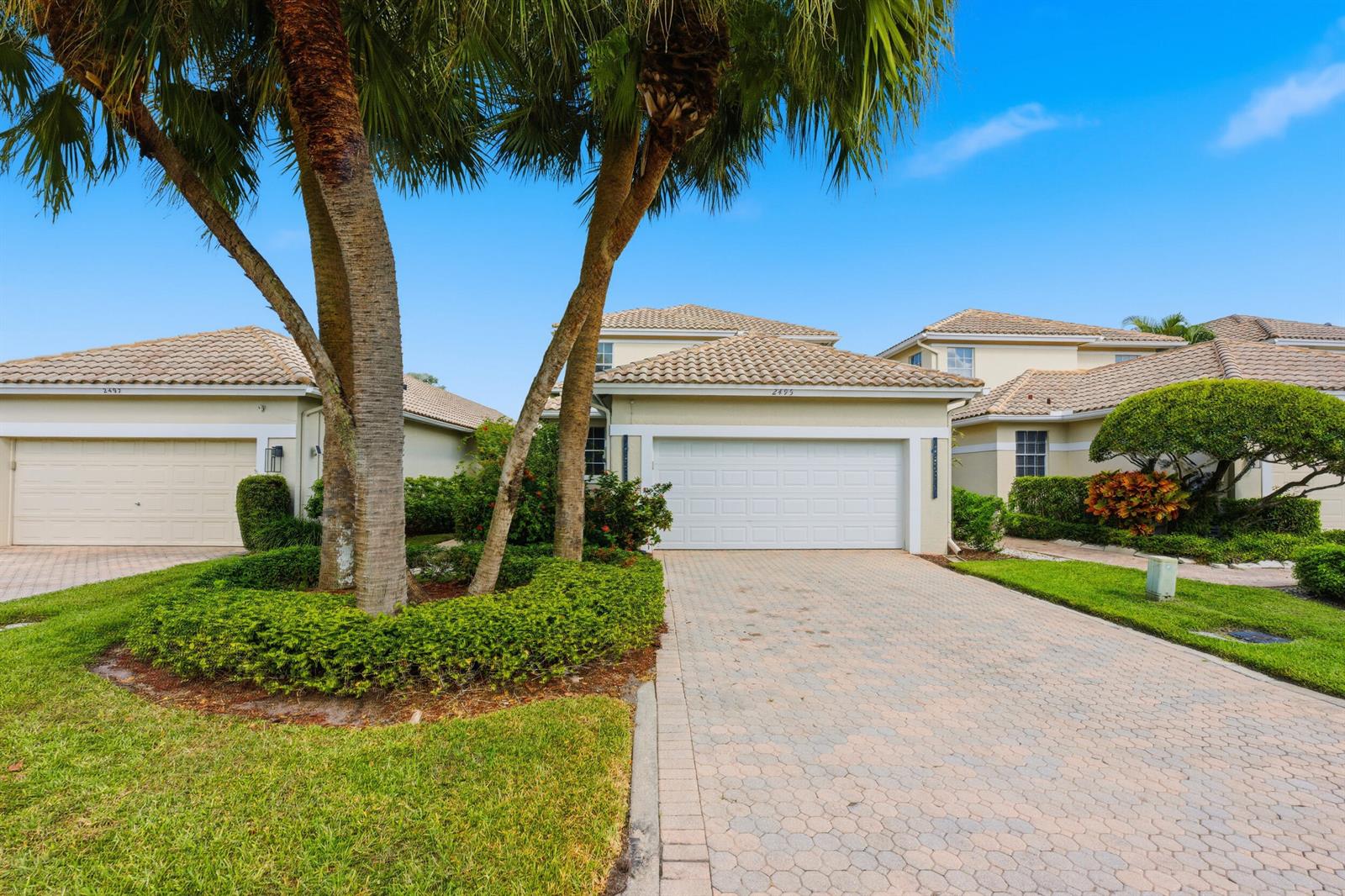 A paved driveway leads to the two-car garage of a tan house with palm trees — 2495 NW 66th Drive, Boca Raton FL 33496, BOCA RATON, FL