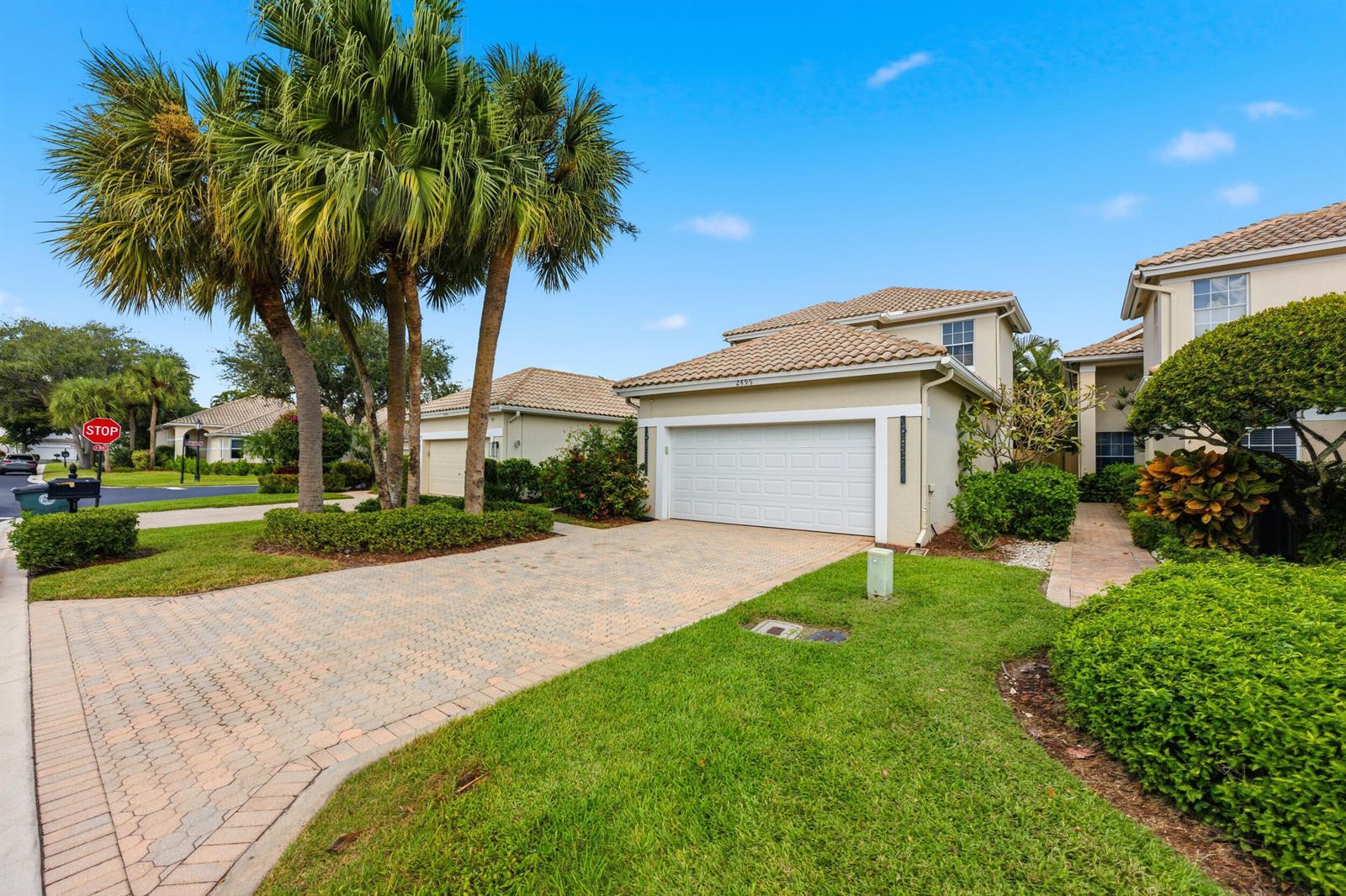 A paved driveway leads to a two-car garage of a tan house with palm trees — 2495 NW 66th Drive, Boca Raton FL 33496, BOCA RATON, FL
