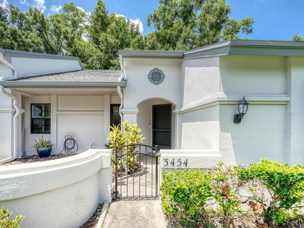 A white stucco house exterior features a gated entryway and a house number 3454 — 3454 KILLDEER PLACE, PALM HARBOR, FL