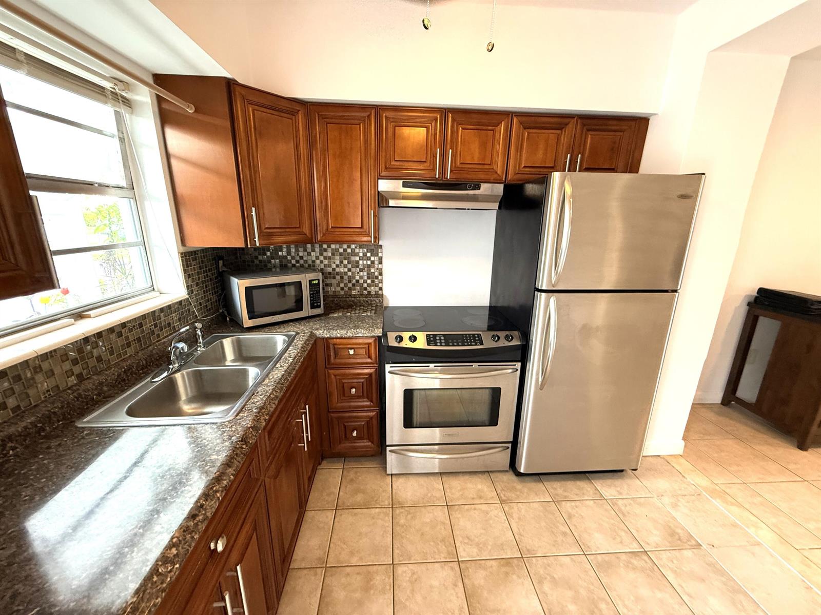 A kitchen features wood cabinets, stainless steel appliances, a tiled backsplash, and tile flooring — 6560 Winfield Boulevard # 102, Margate FL 33063, MARGATE, FL