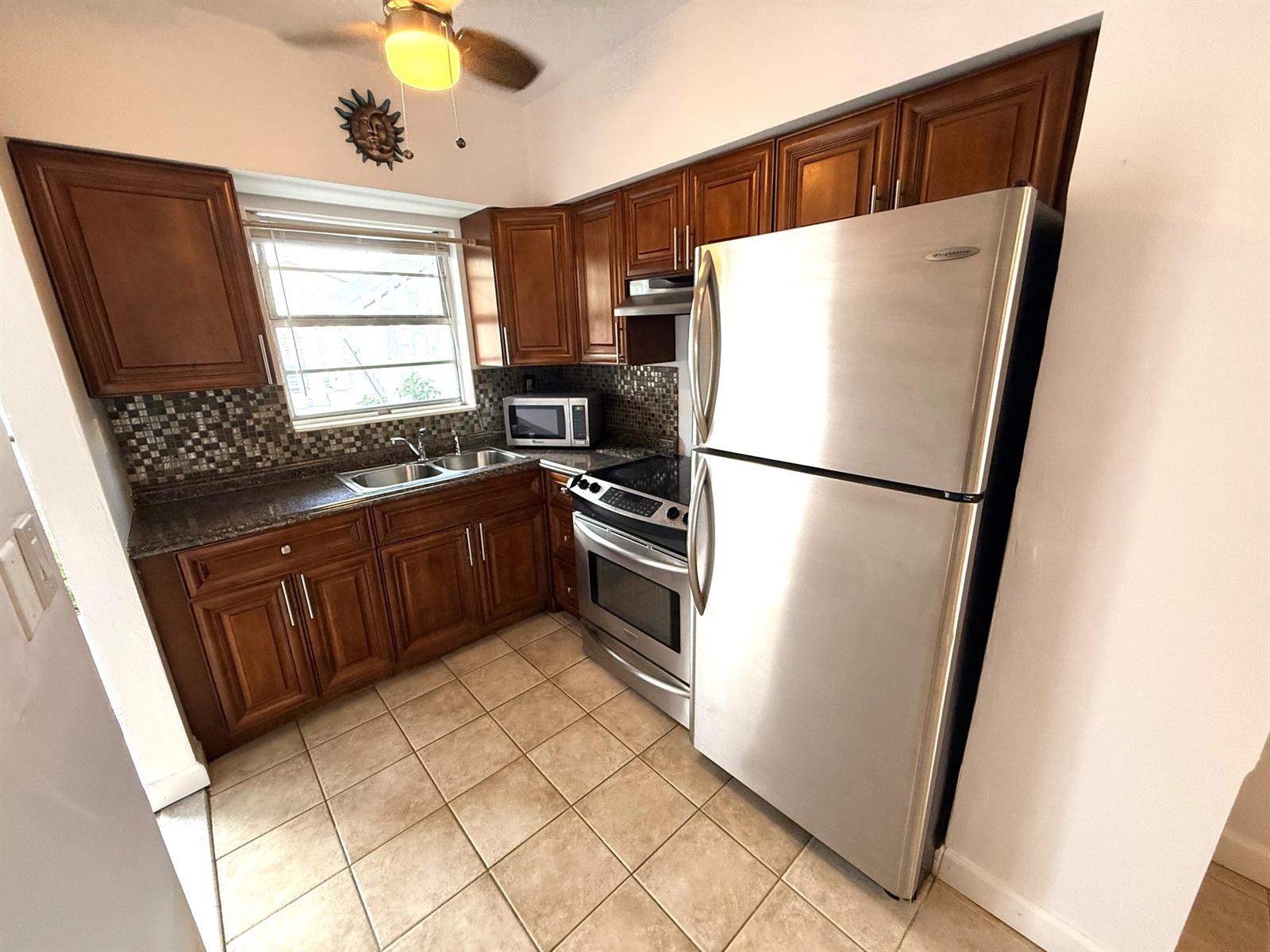 A kitchen features wood cabinets, stainless steel appliances, a tiled backsplash, and light floor tiles — 6560 Winfield Boulevard # 102, Margate FL 33063, MARGATE, FL