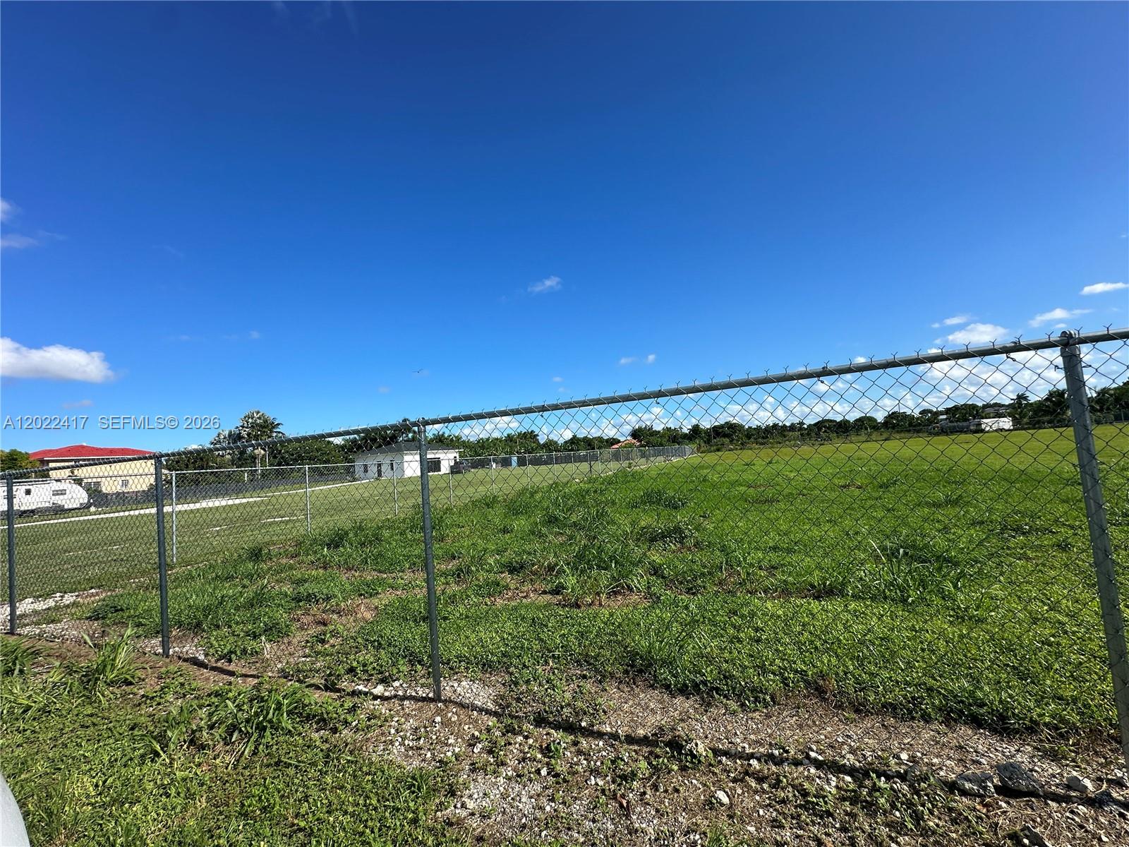 A chain-link fence encloses a large, grassy vacant lot under a clear blue sky — 19690 SW 206th St, Miami FL 33187, MIAMI, FL