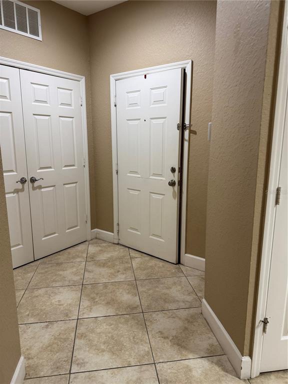 An entryway features beige walls, tiled flooring, a double-door closet, and a white front door — 6335 CONTESSA DRIVE UNIT 107, ORLANDO, FL