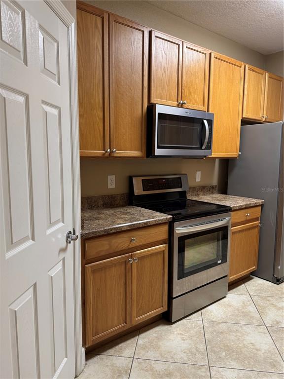 A kitchen features wood cabinets, stainless steel appliances, and tile flooring — 6335 CONTESSA DRIVE UNIT 107, ORLANDO, FL