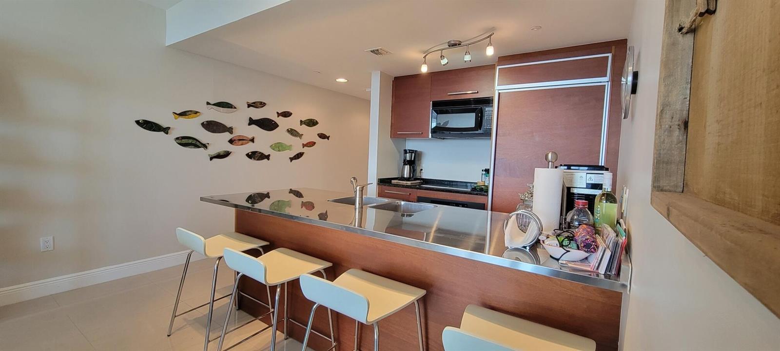 A kitchen features a stainless steel countertop island, bar seating, and wooden cabinetry — 1850 S Ocean Drive # 3806, Hallandale Beach FL 33009, HALLANDALE BEACH, FL