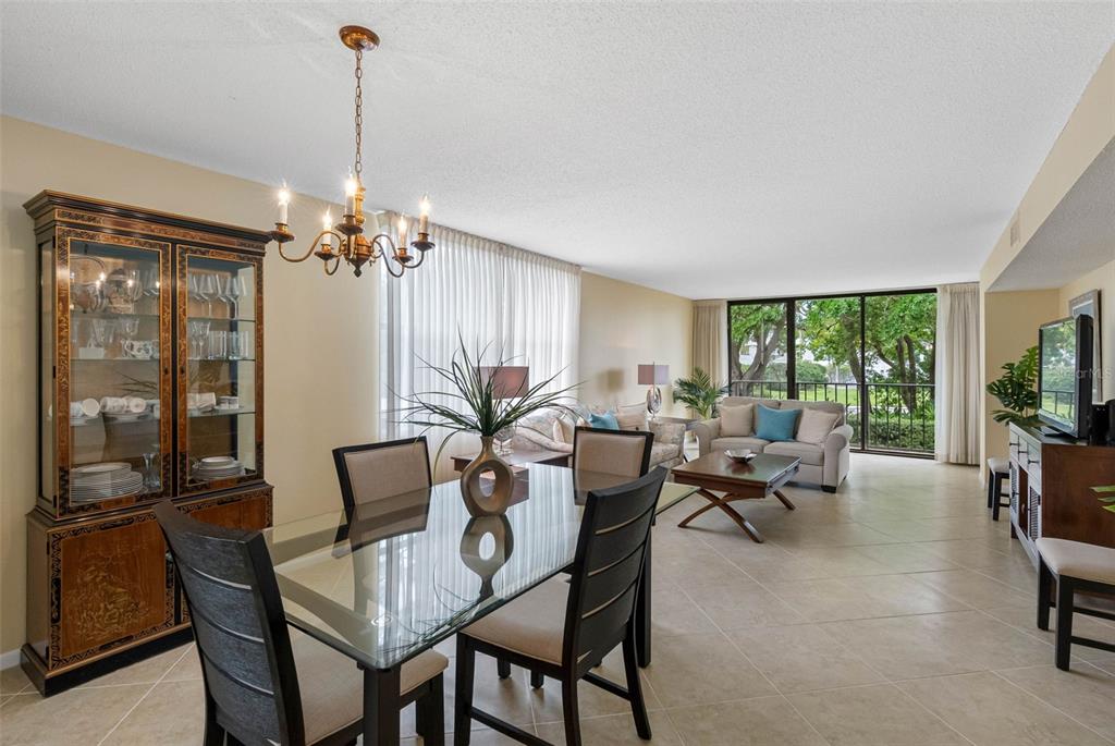 An open-concept living and dining area features tile flooring, a glass dining table, and balcony views — 100 OAKMONT LANE UNIT 203, BELLEAIR, FL