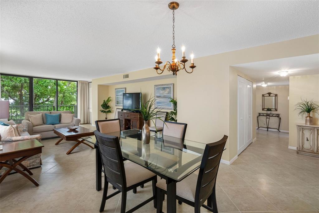 A dining area with a glass table and chandelier opens into a living room — 100 OAKMONT LANE UNIT 203, BELLEAIR, FL