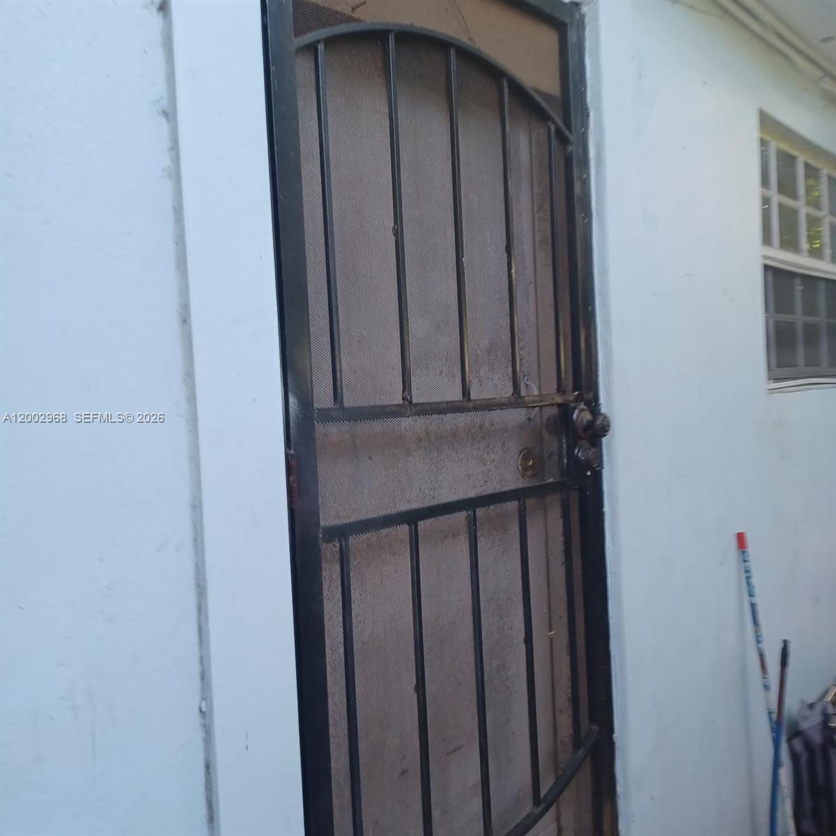 A black metal security screen door is installed on the exterior of a white building — 5250 NW 24th Ave, Miami FL 33142, MIAMI, FL