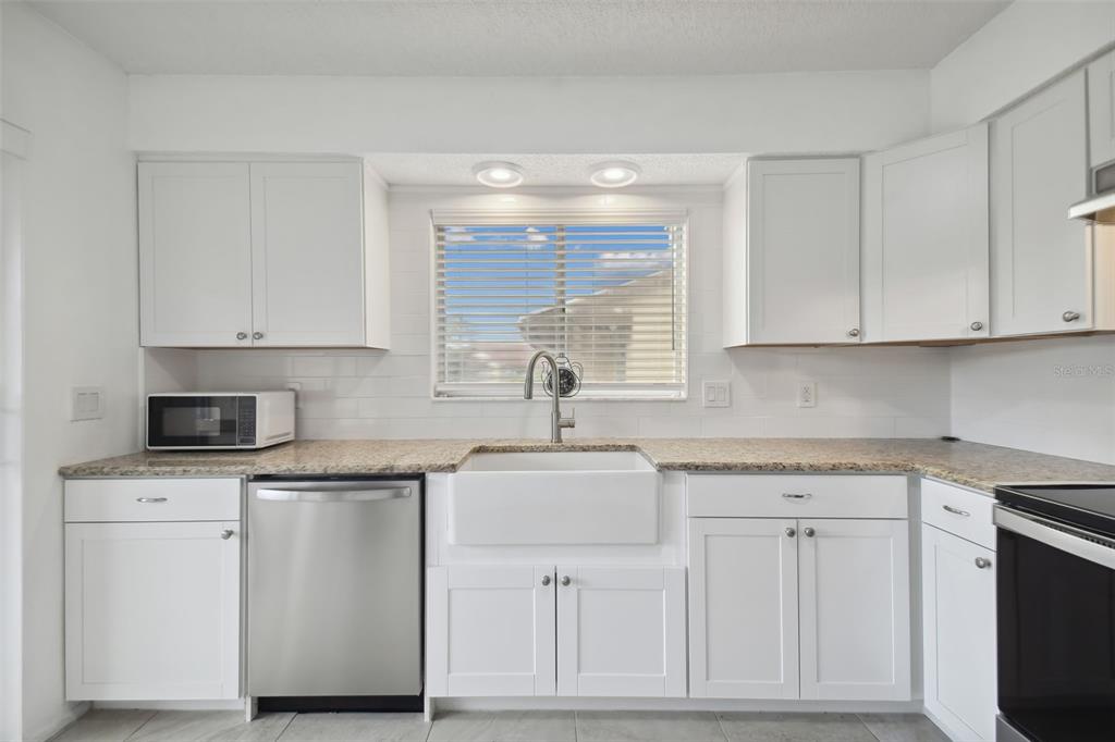 A kitchen with white cabinets, granite countertops, a farmhouse sink, and stainless steel appliances — 4028 DAVIT DRIVE UNIT 4028, NEW PORT RICHEY, FL