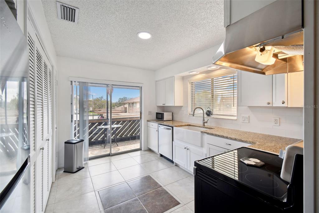 A kitchen features white cabinets, granite countertops, a farmhouse sink, and a sliding glass door — 4028 DAVIT DRIVE UNIT 4028, NEW PORT RICHEY, FL
