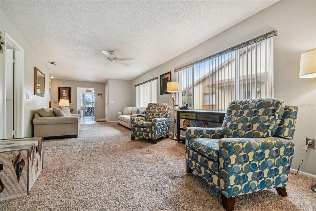 A living room features beige carpeting, two patterned armchairs, a sofa, and large windows — 4028 DAVIT DRIVE UNIT 4028, NEW PORT RICHEY, FL